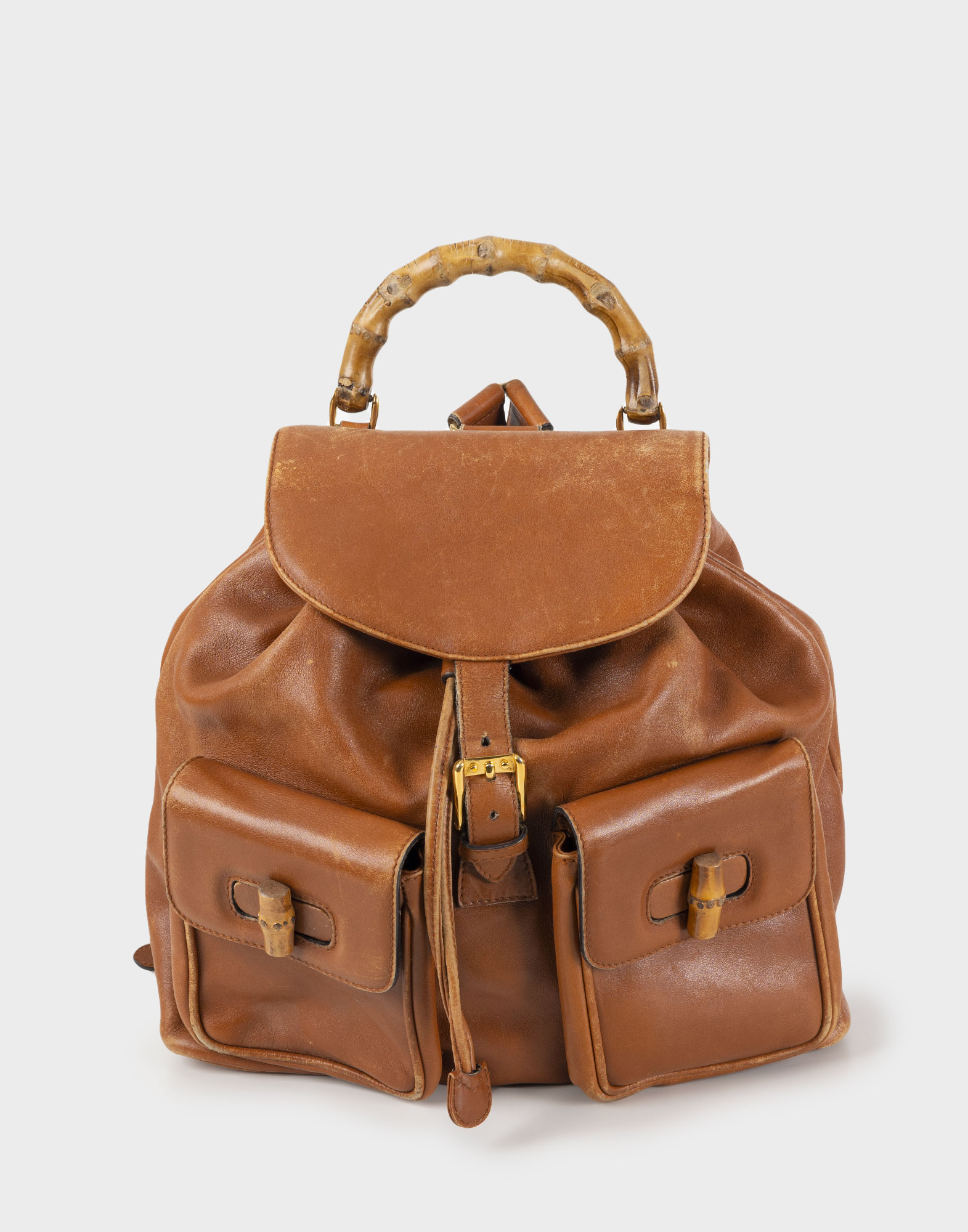 Brown leather backpack with bamboo handle and two pockets. Shot on a gray background.